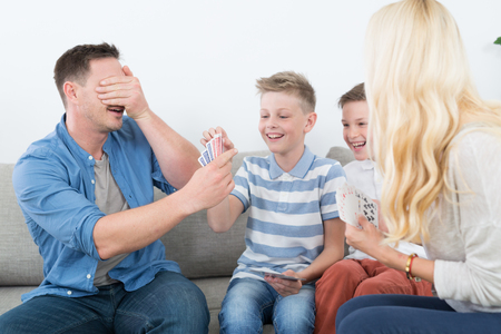 Happy young family playing card game on living room sofa at home. Spending quality leisure time with children and family concept.の写真素材