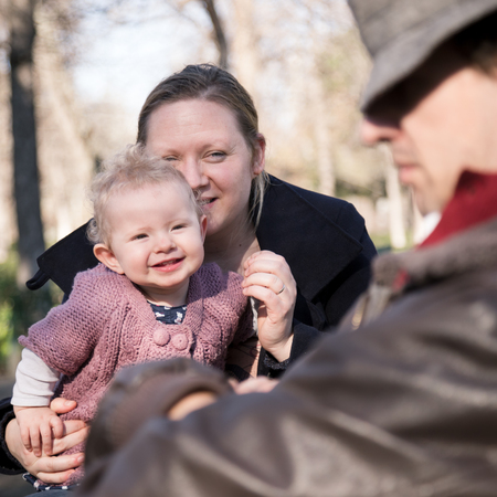 Young happy family with cheerful child having fun in park on sunny day. Tired father napping on the bench.の写真素材