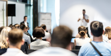 Business and entrepreneurship symposium. Speaker giving a talk at business meeting. Audience in conference hall. Rear view of unrecognized participant in audience.の写真素材