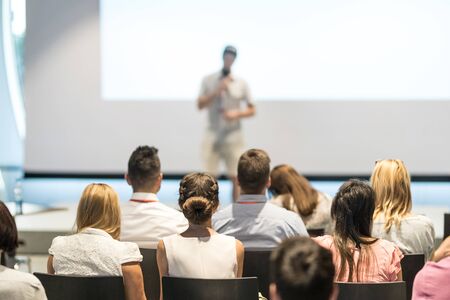 Business and entrepreneurship symposium. Speaker giving a talk at business meeting. Audience in conference hall. Rear view of unrecognized participant in audience.の写真素材