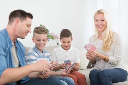 Happy young family playing card game on living room sofa at home. Spending quality leisure time with children and family concept. Cards are generic and debranded.の写真素材