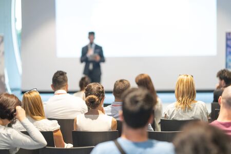 Male speaker giving a talk in conference hall at business event. Audience at the conference hall. Business and Entrepreneurship concept. Focus on unrecognizable people in audience.の写真素材