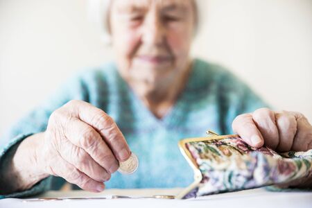 Elderly 96 years old woman sitting miserably at the table at home and counting remaining coins from...