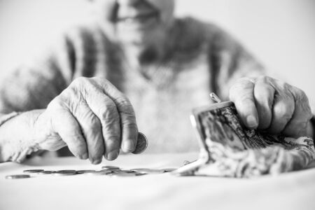 Closeup photo of elderly 96 years old womans hands counting remaining coins from pension in wallet after paying bills. Unsustainability of social transfers and pension system. Black and white.の写真素材