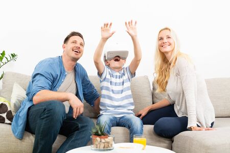 Happy caucasian family at home on living room sofa having fun playing games using virtual reality...