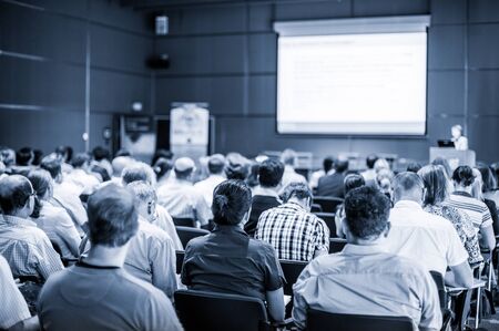 Speaker giving talk at business event. Audience at the conference hall. Business and Entrepreneurship concept. Focus on unrecognizable people in audience. Blue toned grayscale image.の写真素材