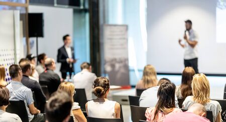 Business and entrepreneurship symposium. Speaker giving a talk at business meeting. Audience in conference hall. Rear view of unrecognized participant in audience.の写真素材
