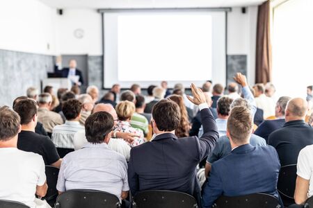 I have a question. Group of business people sitting at the chairs in conference hall. Businessman raising his arm. Conference and Presentation. Business and Entrepreneurship.の写真素材
