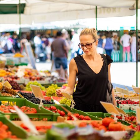Woman buying fruits and vegetables at local food market. Market stall with variety of organic vegetable.の写真素材