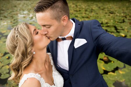 Wedding selfie. Bride and groom kissing passionately outdoors in the park. Caucasian happy romantic...