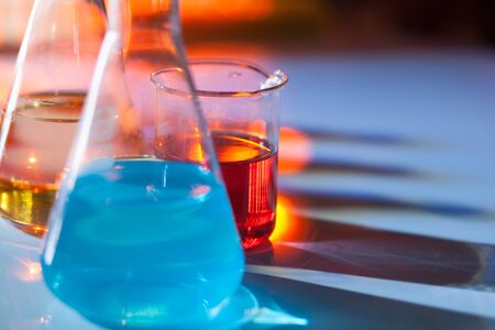 Illuminated laboratory flask filed with colorful chemical solutions with shadows on the table. Laboratory, science, reaserch, chemistry... consept.の写真素材