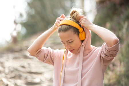 Portrait of beautiful sports woman with hoodie and headphones during outdoors training session. Healthy lifestyle image of young caucasian woman jogging outside.の写真素材