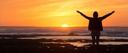 Silhouette of free woman enjoying freedom feeling happy at beach at sunset. Serene relaxing woman in...