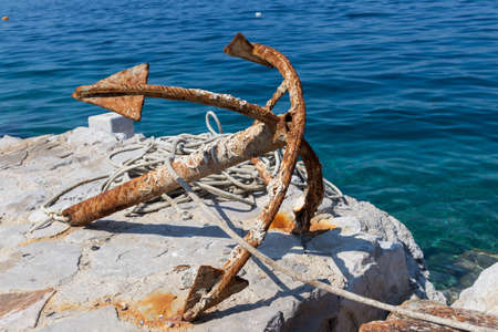 Old rusty anchor on rock by blue adriatic sea.の写真素材