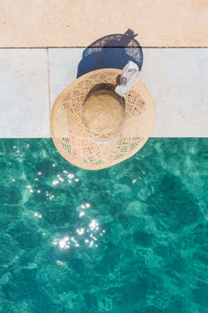 Graphic image of top down view of woman wearing big summer sun hat relaxing on pier by clear...