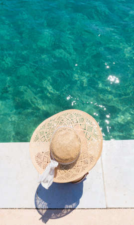 Graphic image of top down view of woman wearing big summer sun hat relaxing on pier by clear turquoise sea.の写真素材
