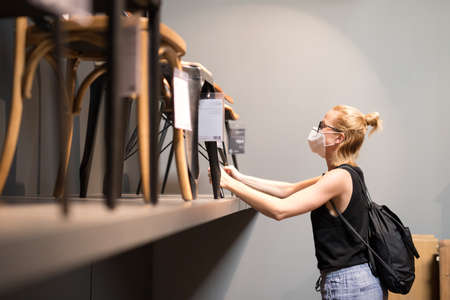 New normal during covid epidemic. Caucasian woman shopping at retail furniture and home accessories store wearing protective medical face mask to prevent spreading of corona virus.の写真素材
