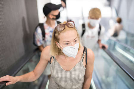 Portrait of casual young woman uses escalators in the department store wearing protective mask as...