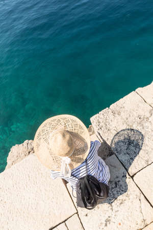 Graphic image of top down view of woman wearing big summer sun hat relaxing on pier by clear turquoise sea.の写真素材