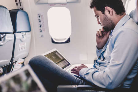 Casually dressed middle aged man working on laptop in aircraft cabin during his business travel. Shallow depth of field photo with focus on businessman eye.の写真素材