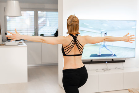 Beautiful blonde woman doing home workout indoors. Woman practice yoga at home. Fit girl using workout tutorials for healthy active lifestyle. Woman using quarantine for home workouts.の写真素材