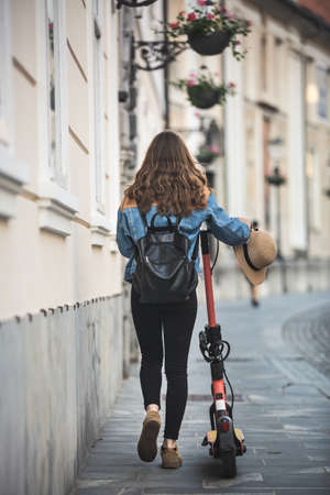 Electro-mobility. Rear view of female traveler exploring old town on environmentally friendly electric scooter.の写真素材