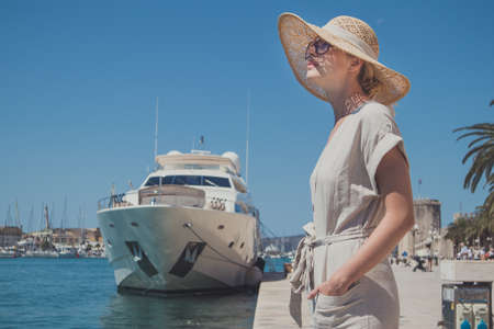 Young woman at the pier with sailing yachts. A beautiful girl enjoing vacation in front of moored...