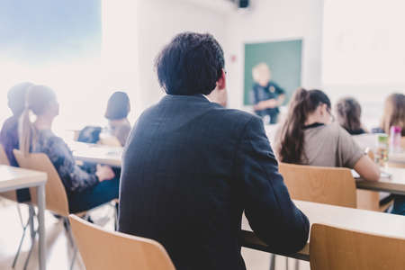Teacher at university in front of a whiteboard screen. Students listening to lecture and making notes.の写真素材