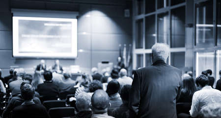 I have a question. Group of business people sitting in conference hall. Businessman raising his arm....