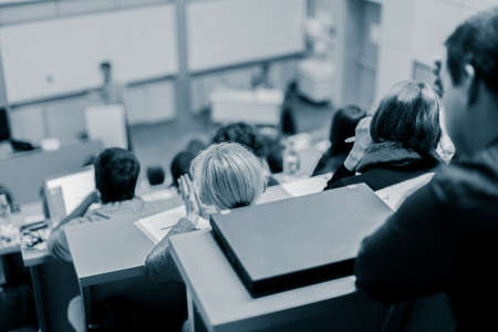 Speaker giving presentation in lecture hall at university. Participants listening to lecture and making notes.の写真素材