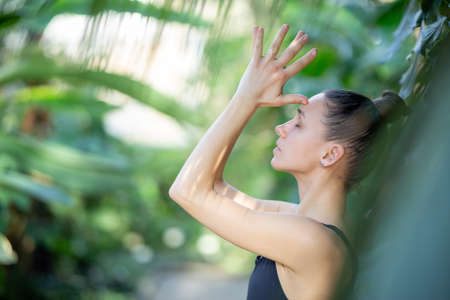 Female meditating and practicing yoga in tropical rainforest. Beautiful young woman practicing yoga outdoor with tropical forest in background.の写真素材