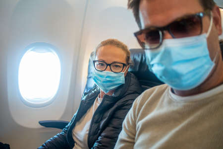 A young couple wearing face masks while traveling on airplane. New normal travel after covid-19 pandemic conceptの写真素材