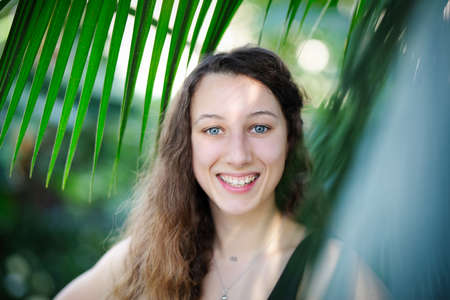 Young beautiful natural cheerful woman with healthy face and skin in exotic greenery. Closeup fresh...