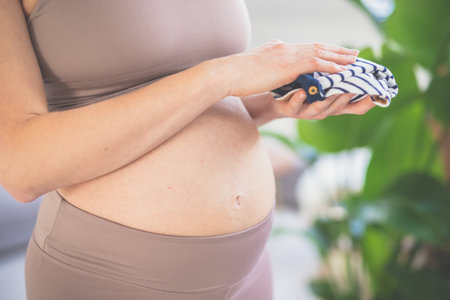 Pregnant woman ready for delivery, holding little clothes for newborn baby. Pregnant woman belly....