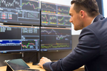 Stock broker trading online while accepting orders by phone. Traders office with multiple computer screens full of index charts and data analysesの写真素材