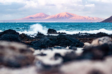 Wild rocky coastline of Fuerteventura and Lanzarote, Canary Islands, Spain. Playa Blanca on Lanzarote with volcano mountain iluminated in sunset seen from Corralejoの写真素材