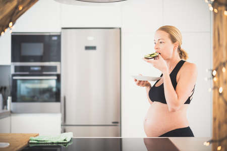 Beautiful sporty fit young pregnant woman having a healthy snack in home kitchen. Healty lifestyle concept.の写真素材