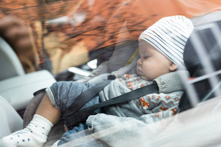 Cute little baby boy sleeping strapped into infant car seat in passenger compartment during car drive.の写真素材