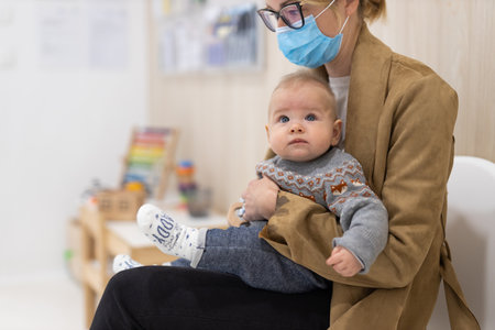 Mother holding infant baby boy in her lap, sitting and waiting in front of doctors office for pediatric well check. childs health care conceptの写真素材