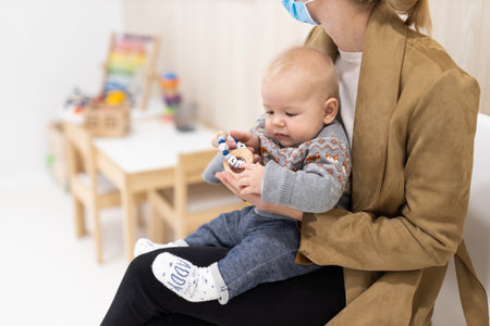 Mother holding infant baby boy in her lap, sitting and waiting in front of doctors office for pediatric well check. childs health care conceptの写真素材