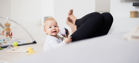 Happy family moments. Mother lying comfortably on childrens mat playing with her baby boy watching...