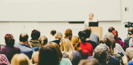 Business and entrepreneurship symposium. Female speaker giving a talk at business meeting. Audience in conference hall. Rear view of unrecognized participant in audience. Copy space on whitescreen.の写真素材