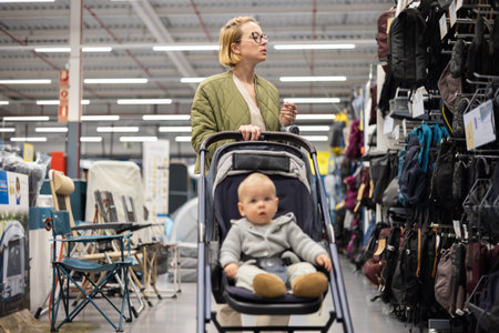 Casualy dressed mother choosing sporty shoes and clothes products in sports department of...