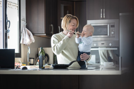 Happy mother and little infant baby boy cooking and tasting healthy dinner in domestic kitchen. Family, lifestyle, domestic life, food, healthy eating and people conceptの写真素材