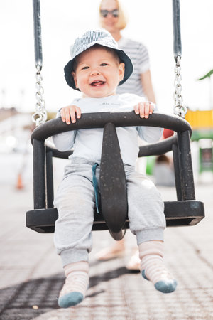 Mother pushing her infant baby boy child on a swing on playground outdoorsの写真素材