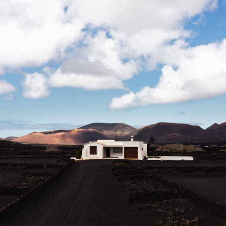 Traditional white house in black volcanic landscape of La Geria wine growing region with view of Timanfaya National Park in Lanzarote. Touristic attraction in Lanzarote island, Canary Islands, Spainの写真素材