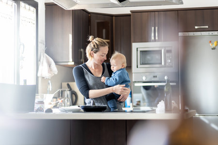 Happy mother and little infant baby boy making pancakes for breakfast together in domestic kitchen. Family, lifestyle, domestic life, food, healthy eating and people conceptの写真素材