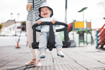Mother pushing her infant baby boy child on a swing on playground outdoorsの写真素材