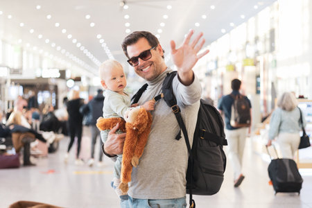 Father traveling with child, holding his infant baby boy at airport terminal waiting to board a plane waving goodby. Travel with kids conceptの写真素材