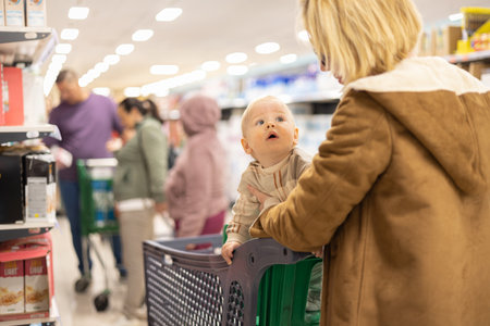 Casualy dressed mother choosing products in department of supermarket grocery store with her infant baby boy child in shopping cartの写真素材